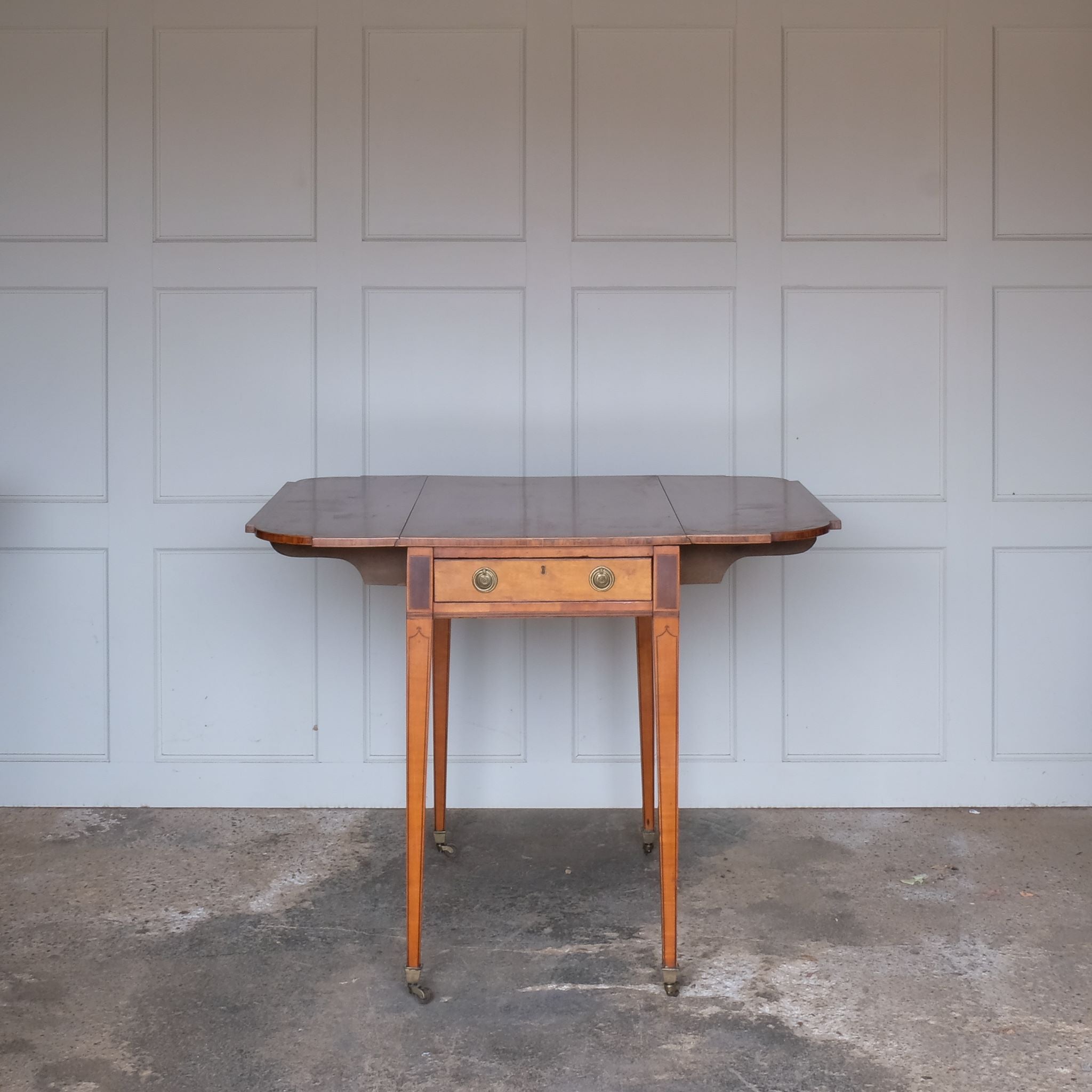 A lovely George III satinwood Pembroke table, the shaped drop leaf top with elegant crossbanding above a single end drawer with a dummy drawer on the opposing side, raised on gently tapering square legs with delicate inlay detailing over brass castors, with some gentle surface patina to the top as is commensurate with age and use, in very good condition