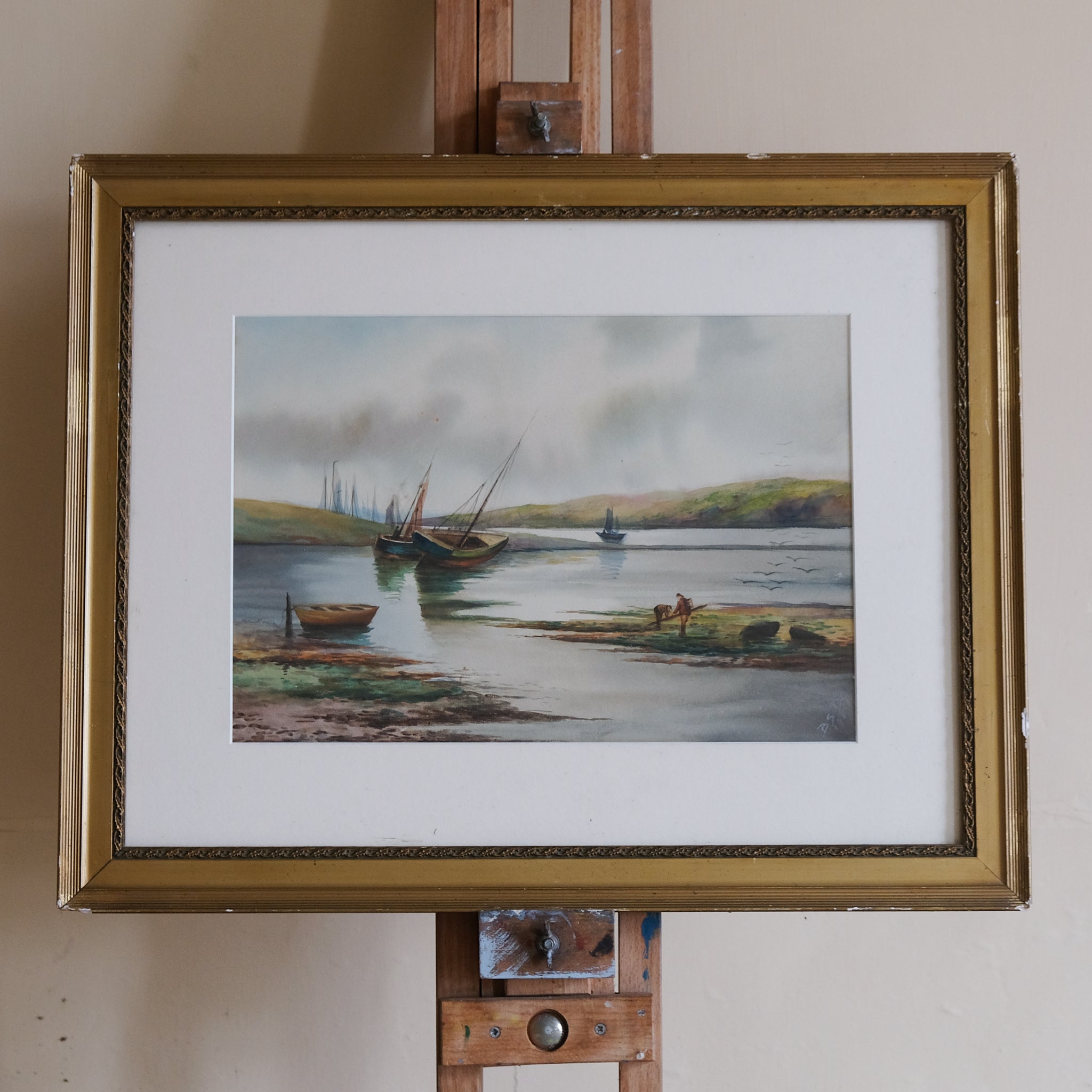 This charming scene is of a river estuary with boat on the shore and in the background, in the foreground at right two figures comb the shore.