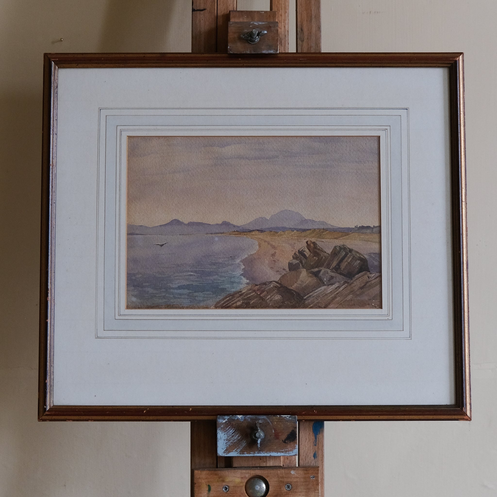 Framed artwork of a coastal scene with mountains in the distance, framed.