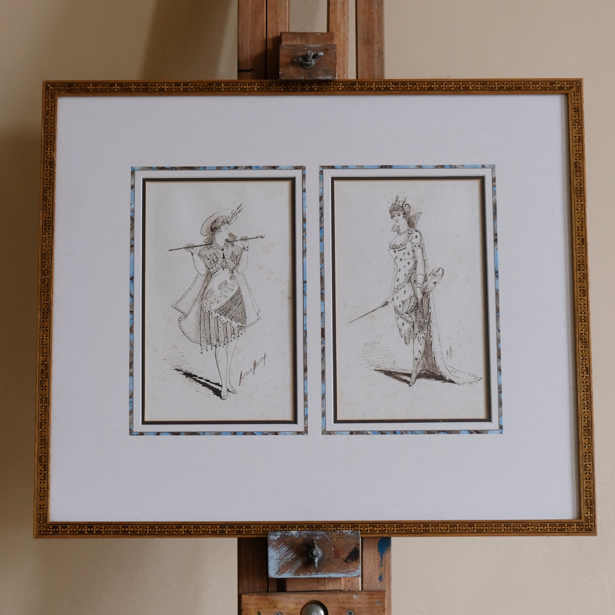 Framed artwork on an easel with two illustrations of women in costume.