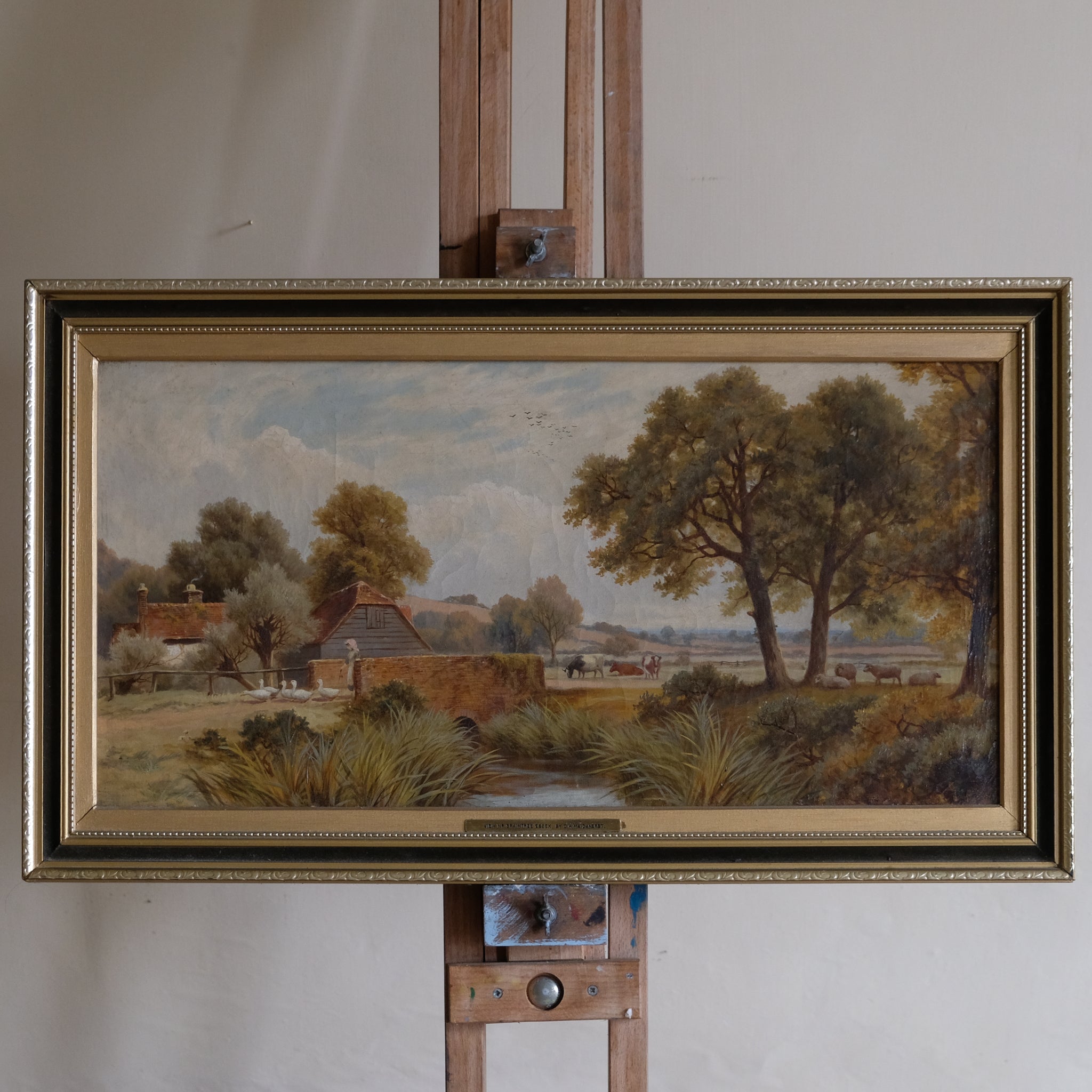 Framed landscape painting on an easel against a plain wall