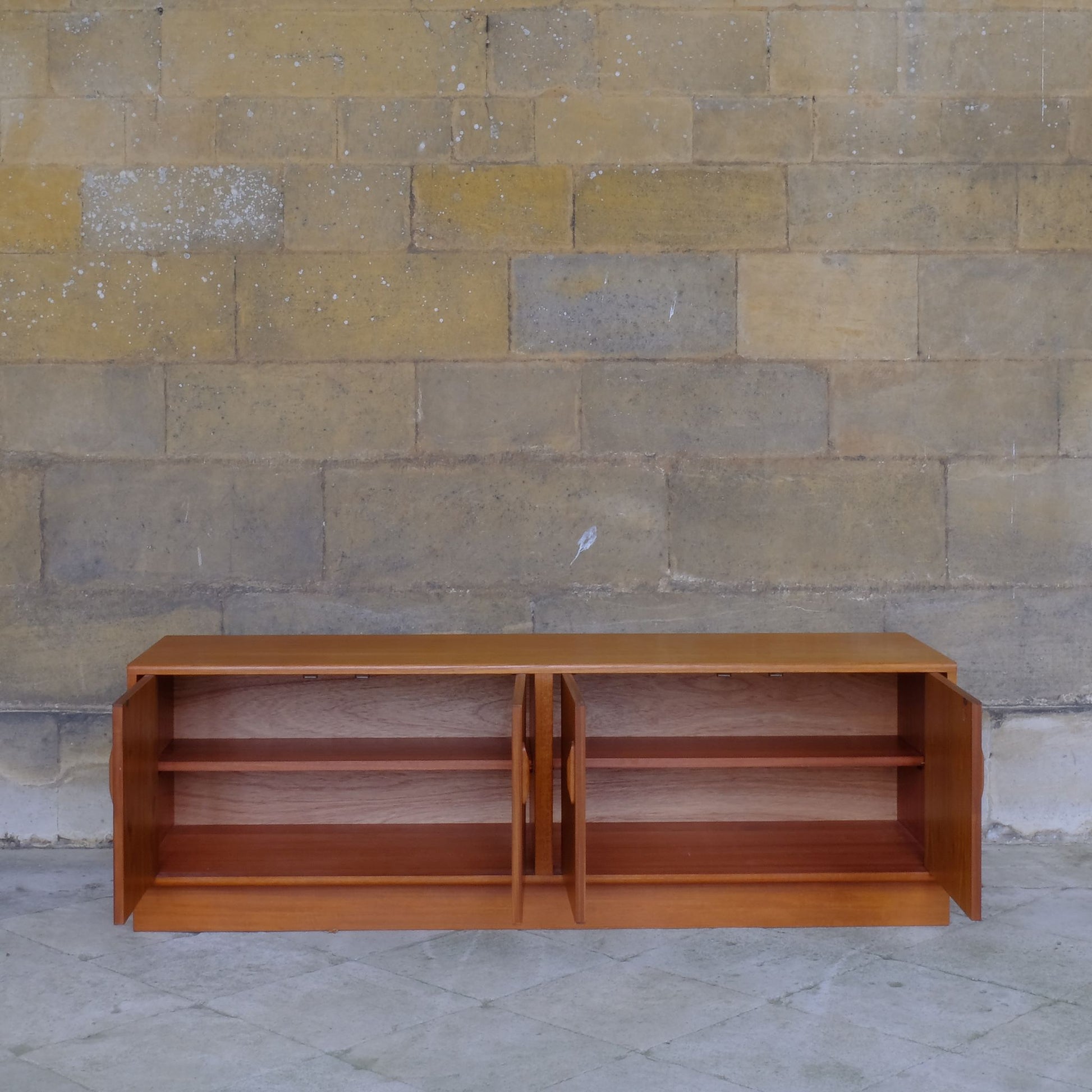 A low teak mid century sideboard by G Plan. Two spacious cabinets, each with a pair of doors and single internal shelf. The maker's mark is present inside one of the doors. In lovely condition, with some very light marks to the top, commensurate with the item's age.