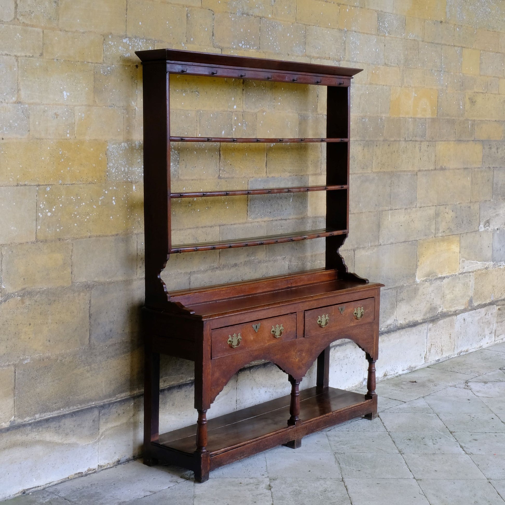 An 18th century dresser in a beautiful rich oak, with open plate shelves over a two drawer base with a twin arched apron on turned legs with a boarded lower shelf. Various hooks along the three shelves and top. Comes in two pieces for easy transport and maneuver. A delightful patina commensurate with age throughout, with some faint signs of an old green tint to the top of the shelves. In very good solid structural condition.