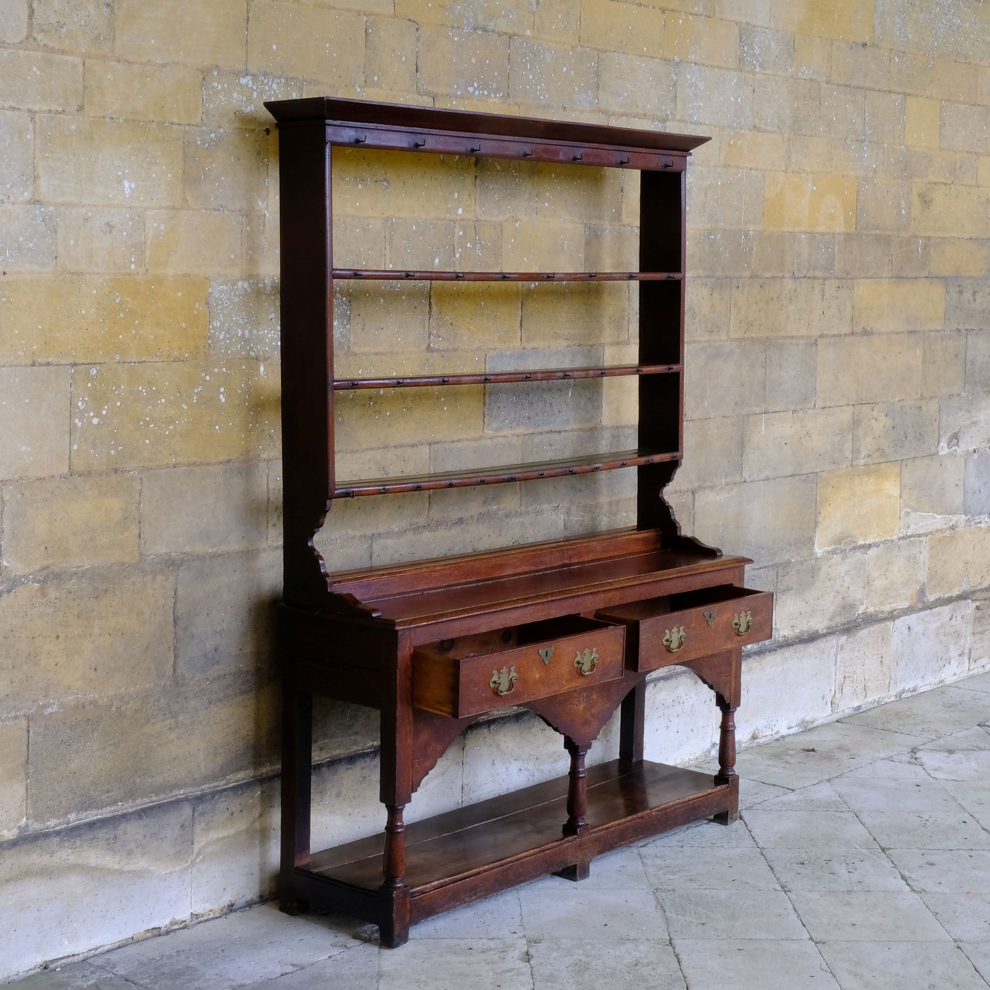 An 18th century dresser in a beautiful rich oak, with open plate shelves over a two drawer base with a twin arched apron on turned legs with a boarded lower shelf. Various hooks along the three shelves and top. Comes in two pieces for easy transport and maneuver. A delightful patina commensurate with age throughout, with some faint signs of an old green tint to the top of the shelves. In very good solid structural condition.