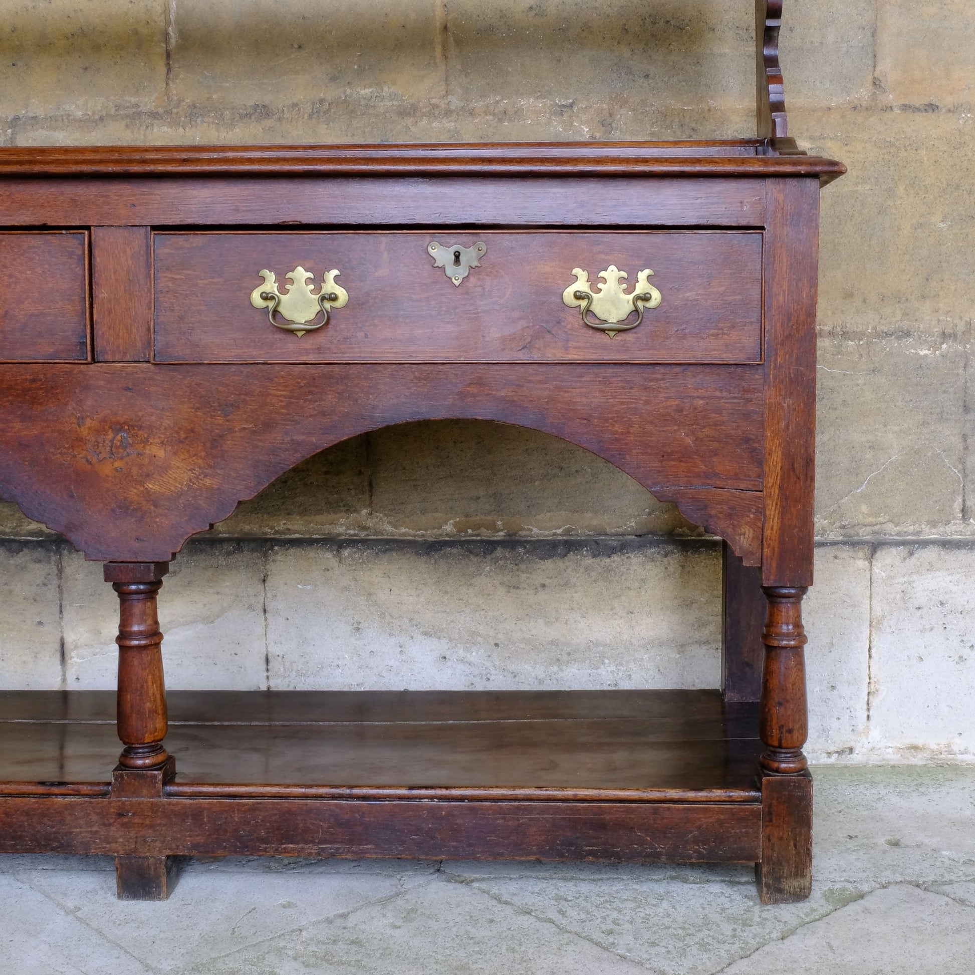 An 18th century dresser in a beautiful rich oak, with open plate shelves over a two drawer base with a twin arched apron on turned legs with a boarded lower shelf. Various hooks along the three shelves and top. Comes in two pieces for easy transport and maneuver. A delightful patina commensurate with age throughout, with some faint signs of an old green tint to the top of the shelves. In very good solid structural condition.