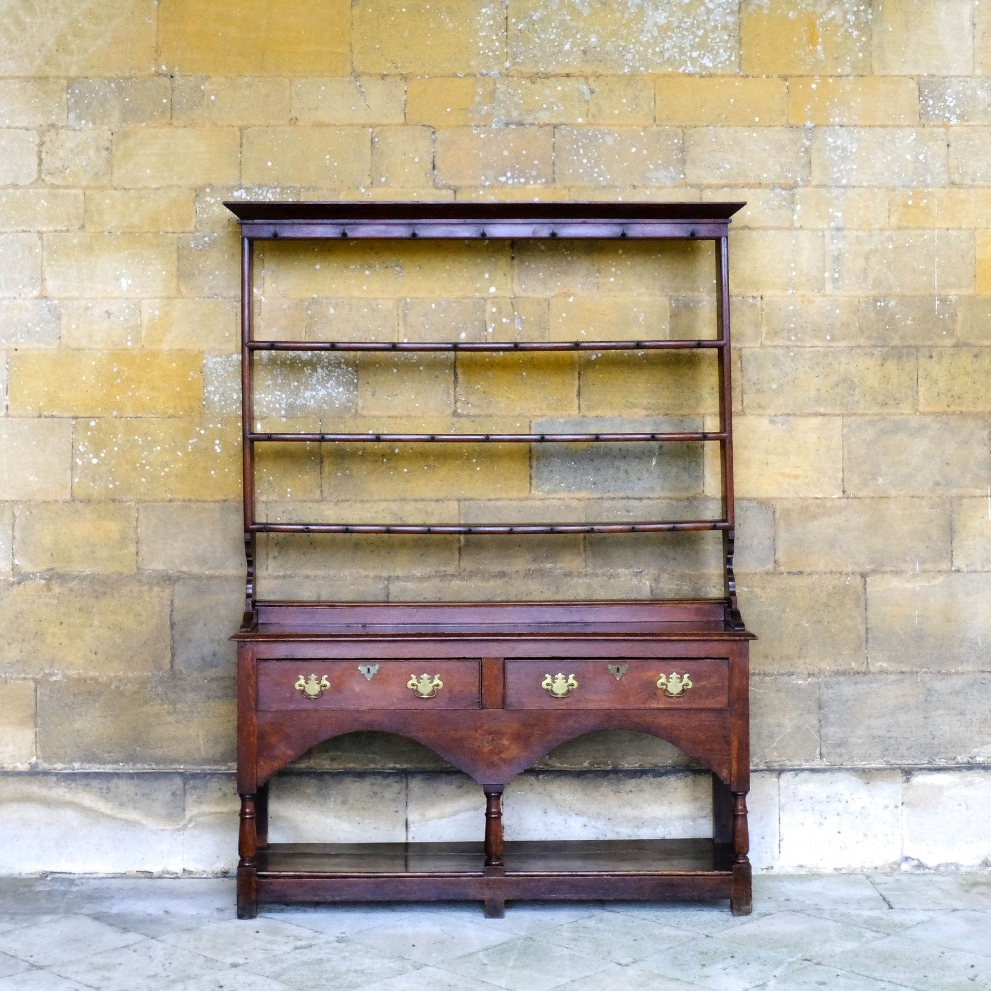 An 18th century dresser in a beautiful rich oak, with open plate shelves over a two drawer base with a twin arched apron on turned legs with a boarded lower shelf. Various hooks along the three shelves and top. Comes in two pieces for easy transport and maneuver. A delightful patina commensurate with age throughout, with some faint signs of an old green tint to the top of the shelves. In very good solid structural condition.