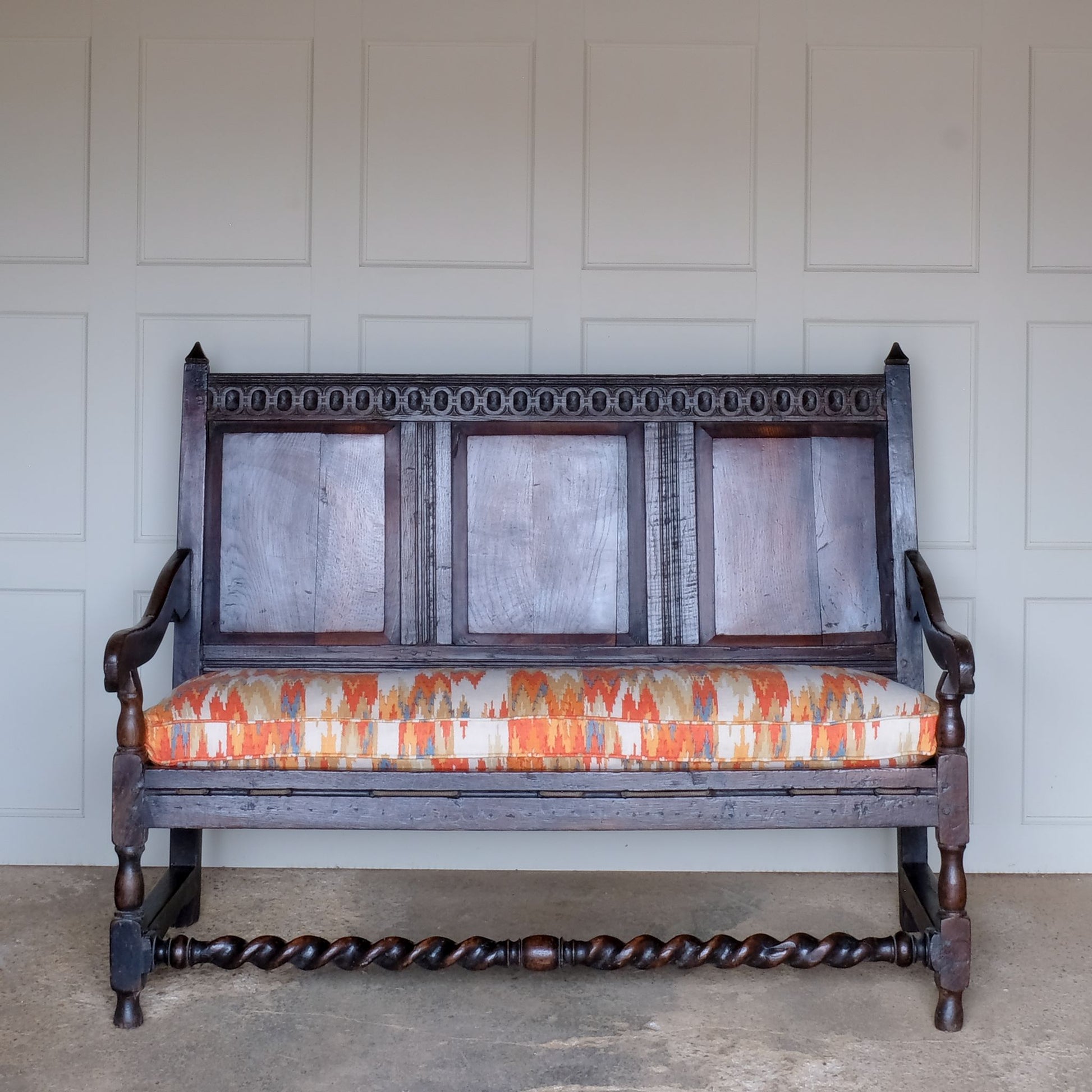 An exquisite 18th century oak settle with a carved back panel on turned legs with a barley twist front stretcher. In good, sturdy condition with a really beautiful, rich patina. The seat has been re-corded, and a new feather cushion made for it, upholstered in "Thika" by Jim Thompson, sourced from Haines Collection. Below this cushion sits a slim pad which has been made to protect the upholstery from wear from the cording.