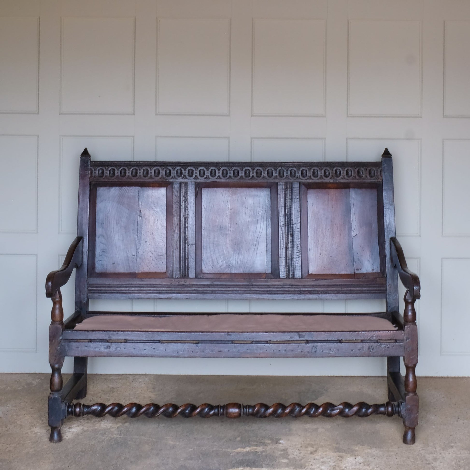 An exquisite 18th century oak settle with a carved back panel on turned legs with a barley twist front stretcher. In good, sturdy condition with a really beautiful, rich patina. The seat has been re-corded, and a new feather cushion made for it, upholstered in "Thika" by Jim Thompson, sourced from Haines Collection. Below this cushion sits a slim pad which has been made to protect the upholstery from wear from the cording.