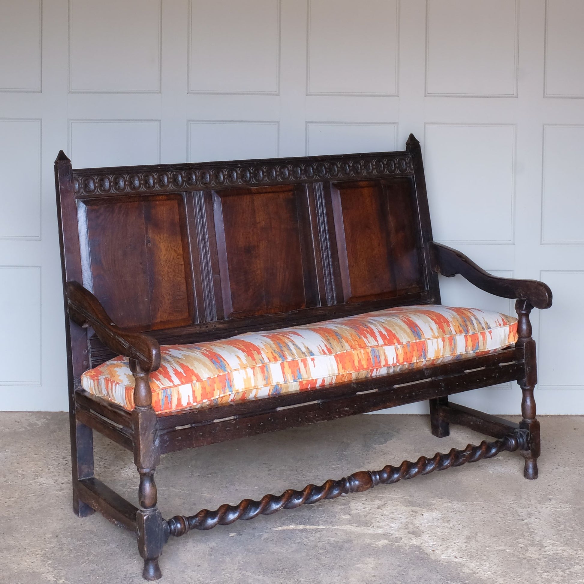 An exquisite 18th century oak settle with a carved back panel on turned legs with a barley twist front stretcher. In good, sturdy condition with a really beautiful, rich patina. The seat has been re-corded, and a new feather cushion made for it, upholstered in "Thika" by Jim Thompson, sourced from Haines Collection. Below this cushion sits a slim pad which has been made to protect the upholstery from wear from the cording.