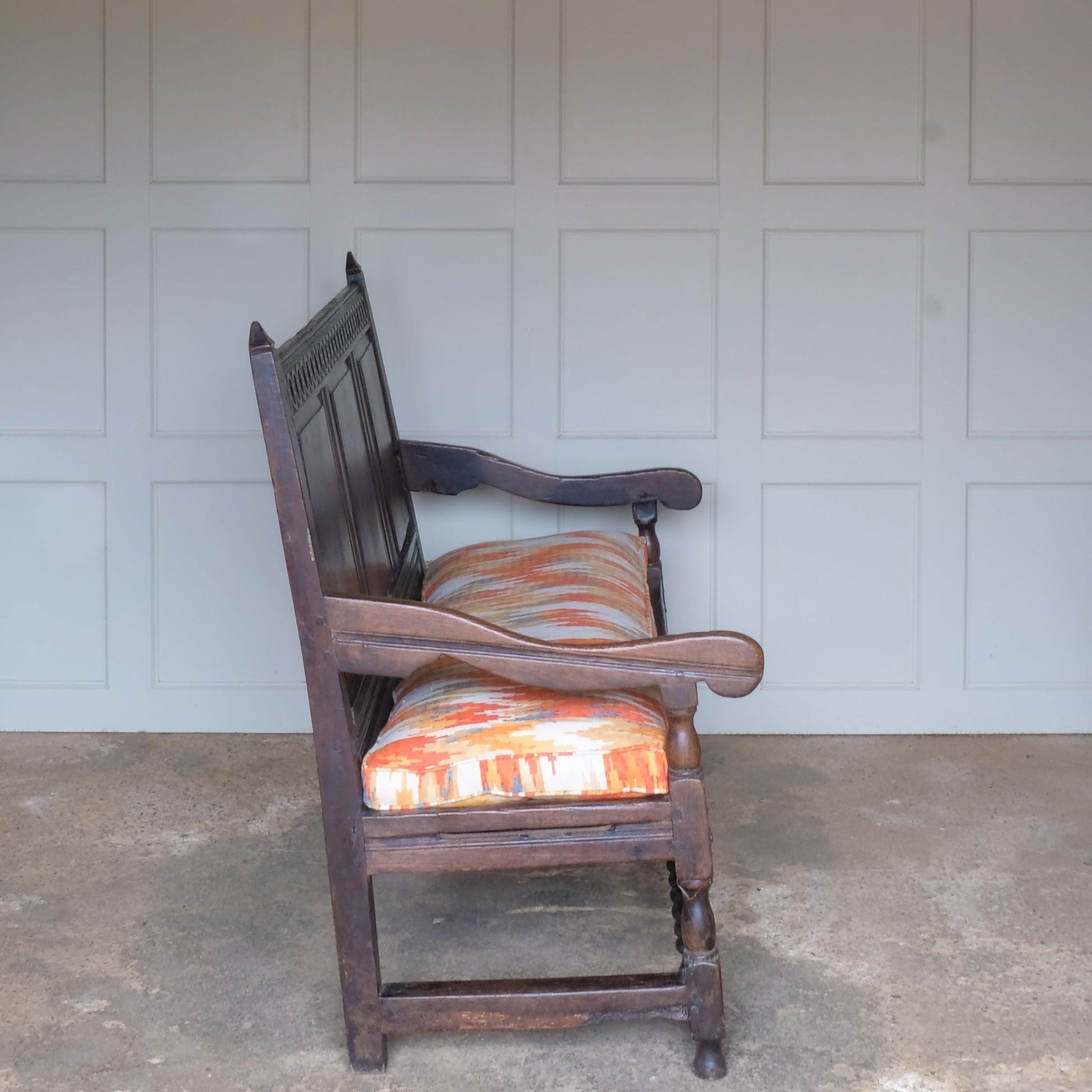 An exquisite 18th century oak settle with a carved back panel on turned legs with a barley twist front stretcher. In good, sturdy condition with a really beautiful, rich patina. The seat has been re-corded, and a new feather cushion made for it, upholstered in "Thika" by Jim Thompson, sourced from Haines Collection. Below this cushion sits a slim pad which has been made to protect the upholstery from wear from the cording.