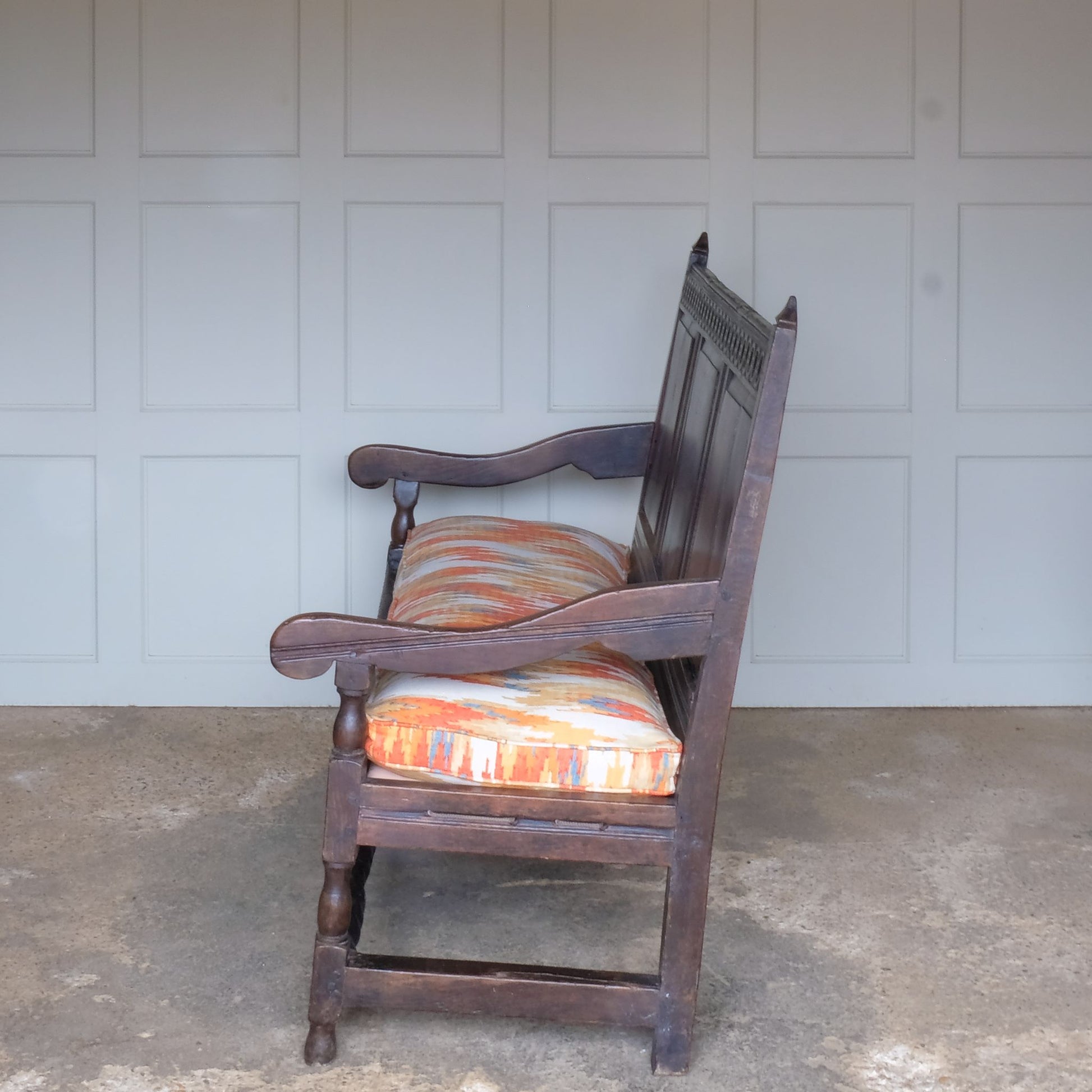 An exquisite 18th century oak settle with a carved back panel on turned legs with a barley twist front stretcher. In good, sturdy condition with a really beautiful, rich patina. The seat has been re-corded, and a new feather cushion made for it, upholstered in "Thika" by Jim Thompson, sourced from Haines Collection. Below this cushion sits a slim pad which has been made to protect the upholstery from wear from the cording.