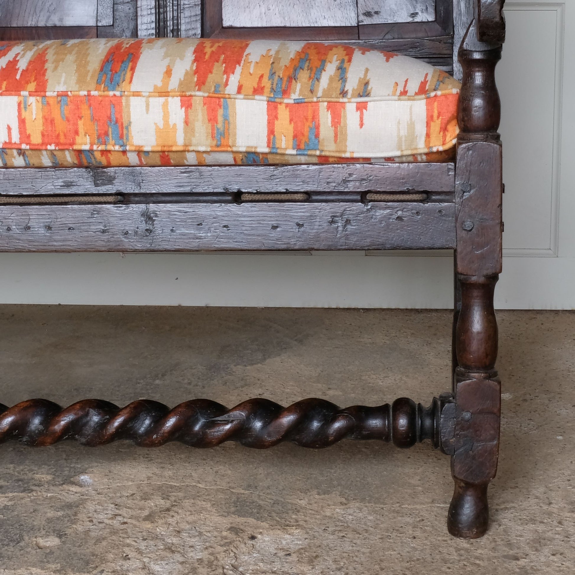 An exquisite 18th century oak settle with a carved back panel on turned legs with a barley twist front stretcher. In good, sturdy condition with a really beautiful, rich patina. The seat has been re-corded, and a new feather cushion made for it, upholstered in "Thika" by Jim Thompson, sourced from Haines Collection. Below this cushion sits a slim pad which has been made to protect the upholstery from wear from the cording.