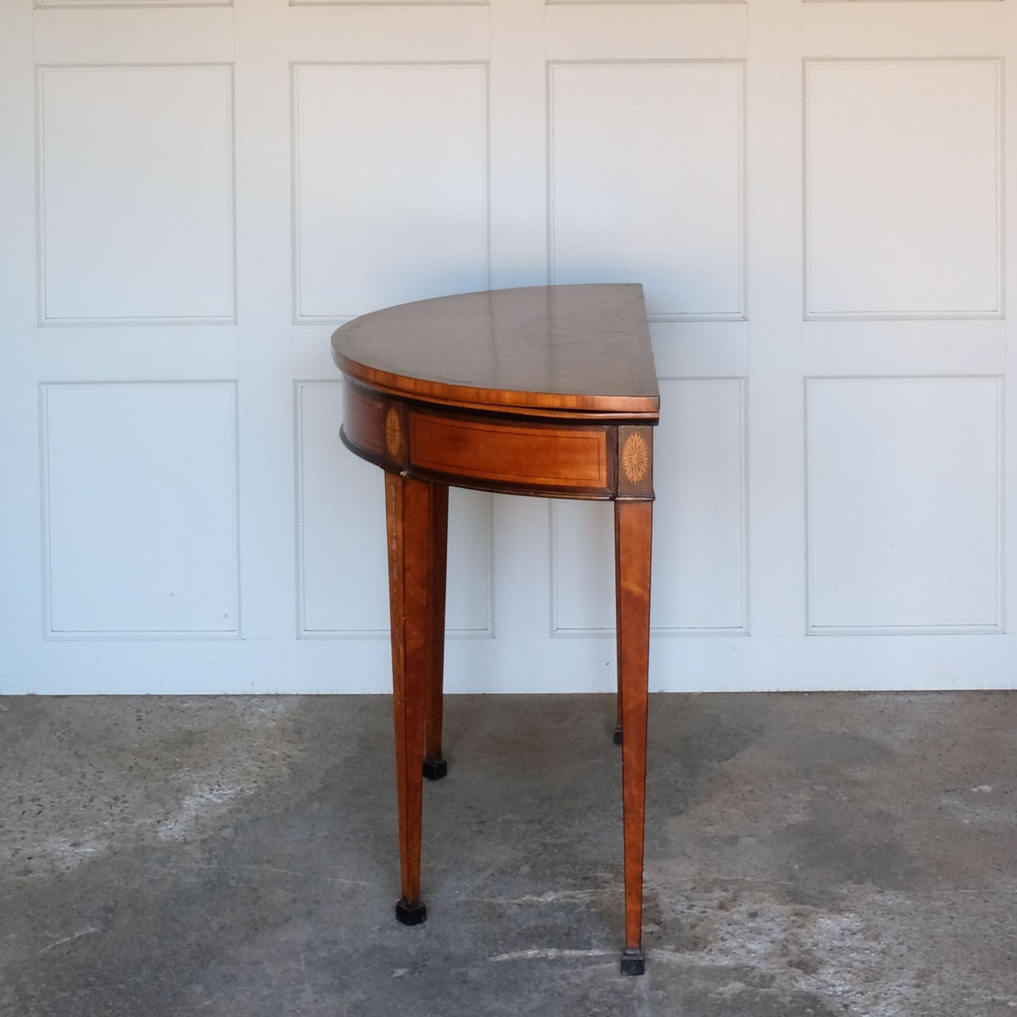 A George III satinwood and marquetry demilune folding card table, with a fold over top fitted with green baize. The top features a beautiful fan inlay and crossbanding around the outside, with the frieze incorporating purple heart crossbanding, over four elegantly tapering legs with floral painted decoration. The rear legs are hinged to swing out and support the folding top. In very good, sturdy overall condition. Would work well as a side console table, or a centre hall table.