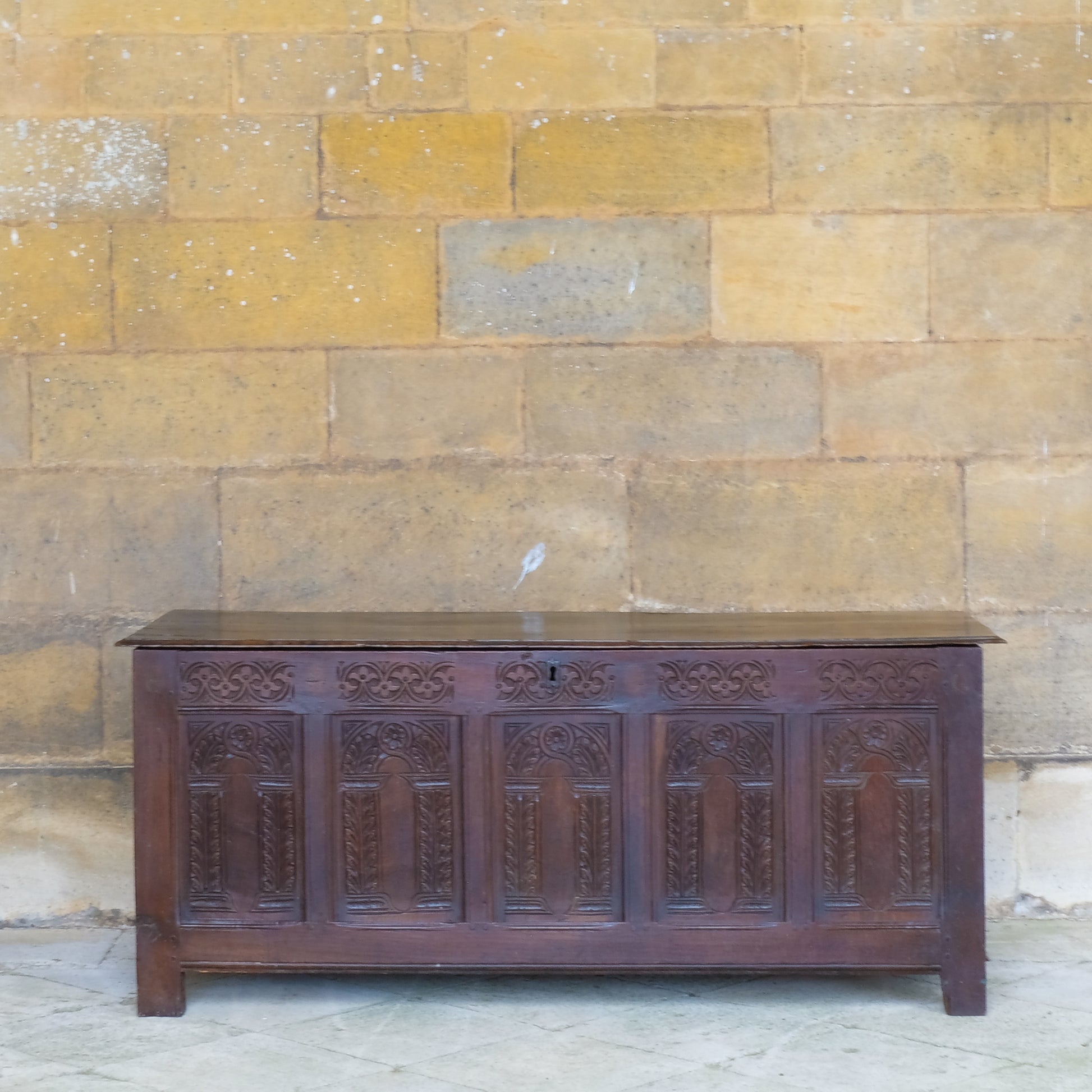 A large 17th century oak coffer with a beautiful five panelled front with stiff leaf carved arcade under a floral top, the moulded rectangular top with the original blacksmith ring hinges. In very good, sturdy condition with a rich patina. Sensitively restored by Anthony Beech, with reclaimed period boards in the base and the top recoloured and waxed. It would be a beautiful storage solution for blankets, toys or a croquet set.