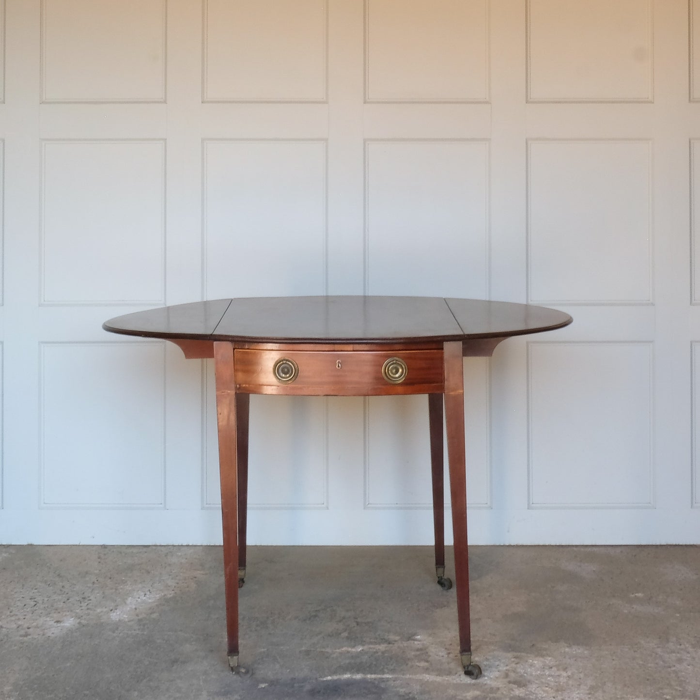 A charming George III mahogany Pembroke table, an oval top with delicate boxwood stringing at the edges over a single drawer, with working key, a dummy drawer matching on the other side, over square tapering legs on brass casters, some minor scuffing to the top and legs commensurate with age, otherwise in very good condition.