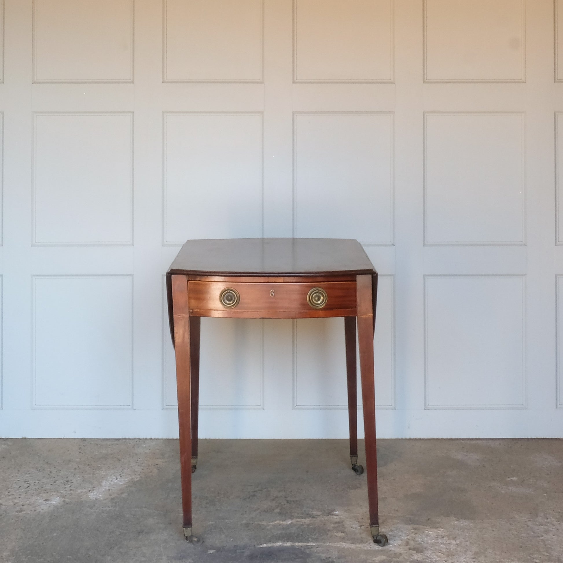 A charming George III mahogany Pembroke table, an oval top with delicate boxwood stringing at the edges over a single drawer, with working key, a dummy drawer matching on the other side, over square tapering legs on brass casters, some minor scuffing to the top and legs commensurate with age, otherwise in very good condition.