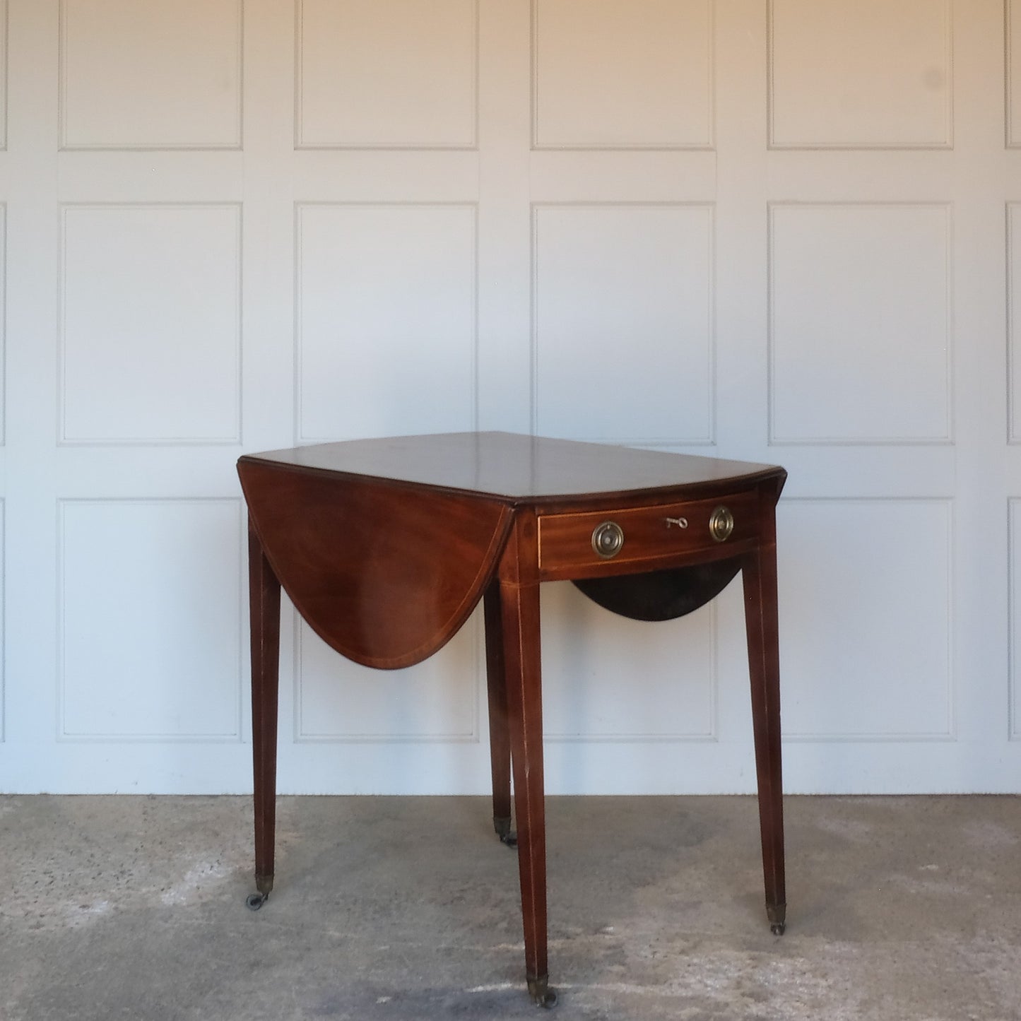 A charming George III mahogany Pembroke table, an oval top with delicate boxwood stringing at the edges over a single drawer, with working key, a dummy drawer matching on the other side, over square tapering legs on brass casters, some minor scuffing to the top and legs commensurate with age, otherwise in very good condition.