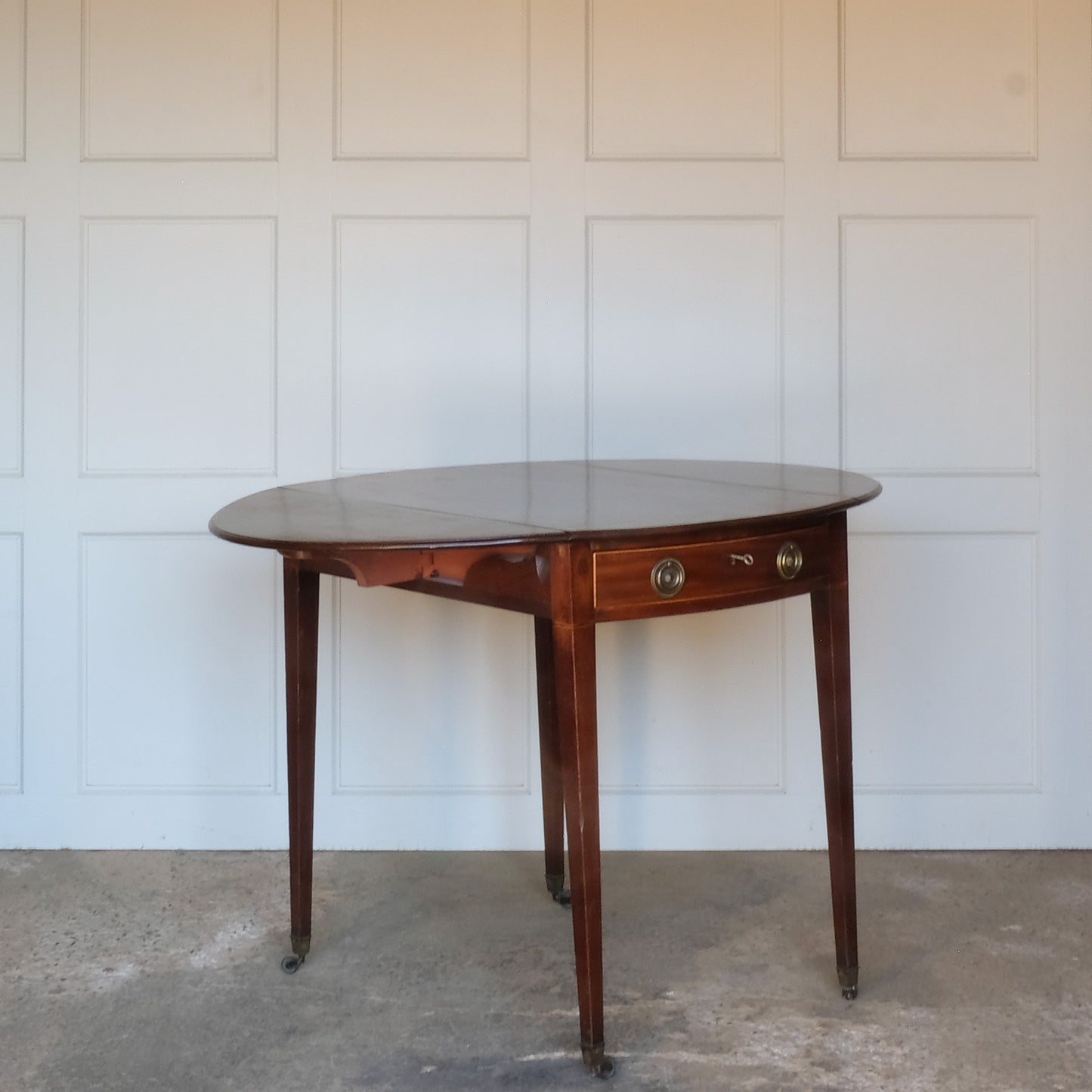 A charming George III mahogany Pembroke table, an oval top with delicate boxwood stringing at the edges over a single drawer, with working key, a dummy drawer matching on the other side, over square tapering legs on brass casters, some minor scuffing to the top and legs commensurate with age, otherwise in very good condition.