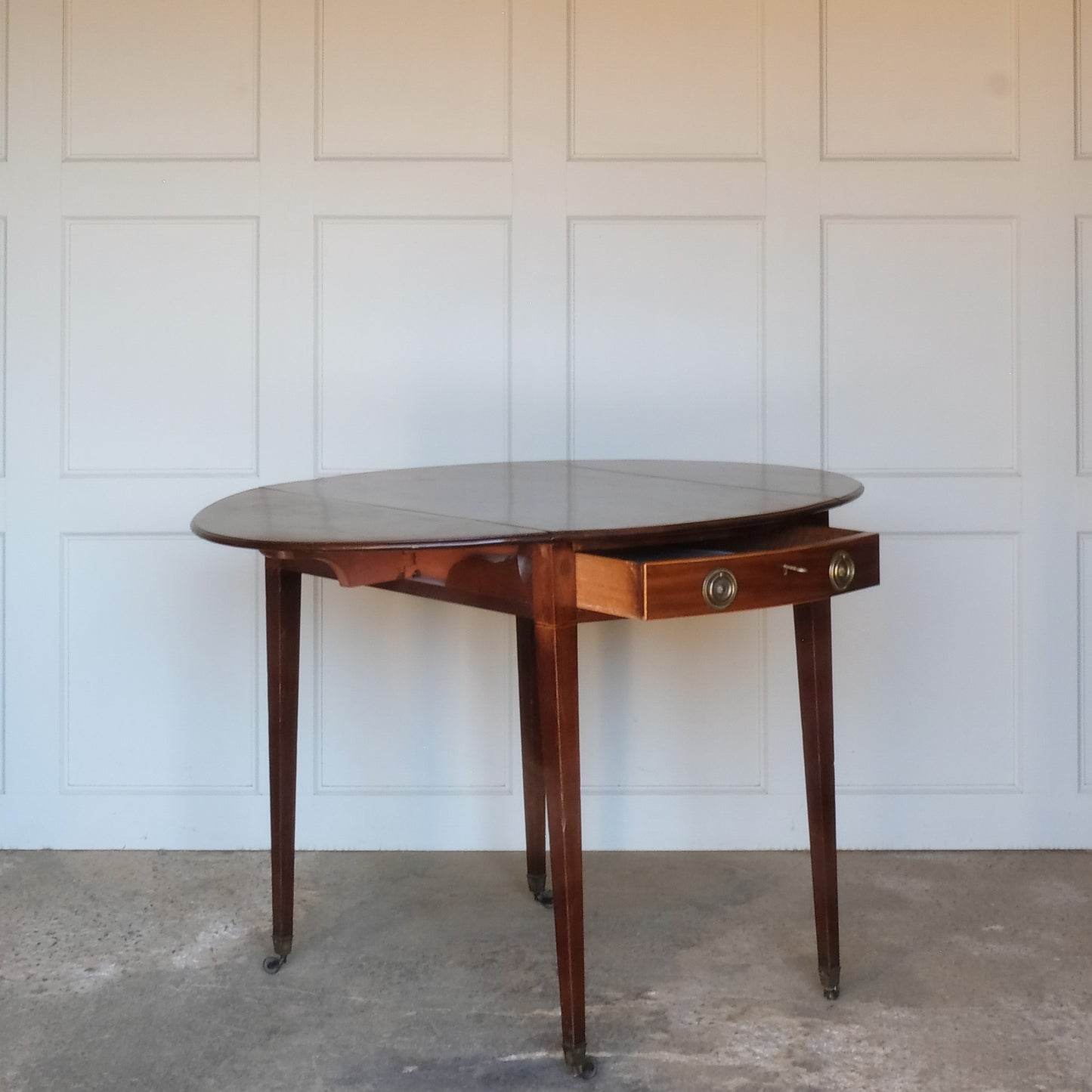 A charming George III mahogany Pembroke table, an oval top with delicate boxwood stringing at the edges over a single drawer, with working key, a dummy drawer matching on the other side, over square tapering legs on brass casters, some minor scuffing to the top and legs commensurate with age, otherwise in very good condition.