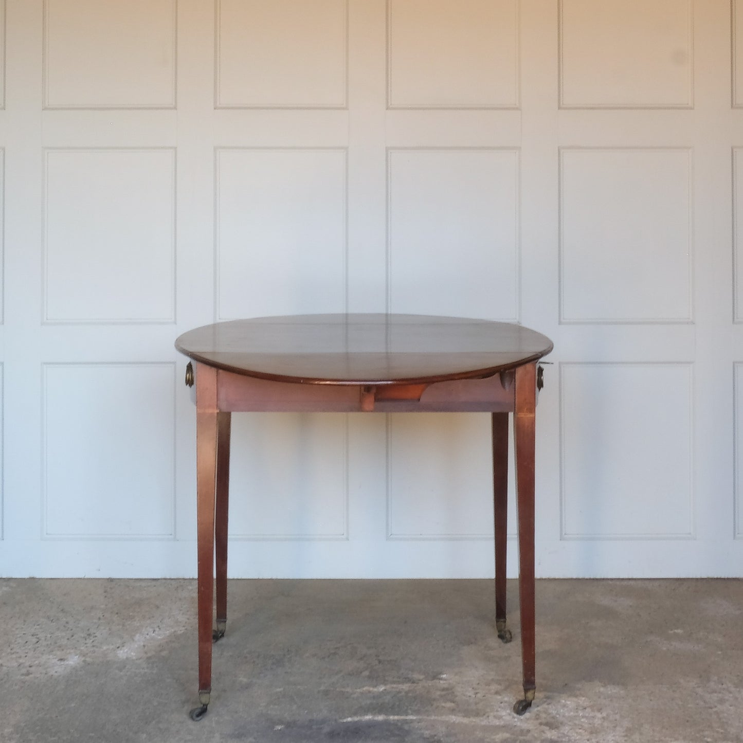 A charming George III mahogany Pembroke table, an oval top with delicate boxwood stringing at the edges over a single drawer, with working key, a dummy drawer matching on the other side, over square tapering legs on brass casters, some minor scuffing to the top and legs commensurate with age, otherwise in very good condition.