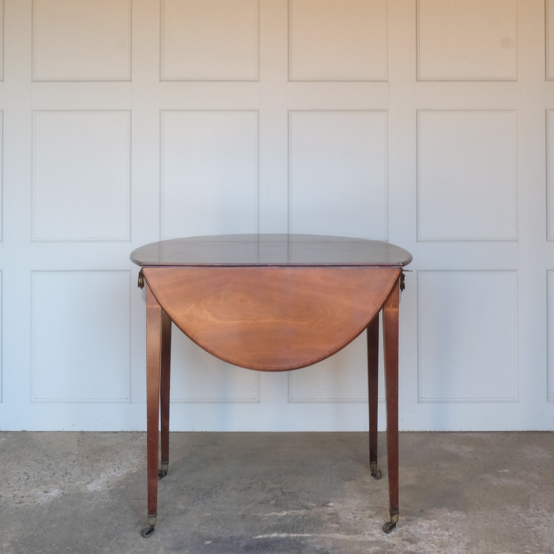 A charming George III mahogany Pembroke table, an oval top with delicate boxwood stringing at the edges over a single drawer, with working key, a dummy drawer matching on the other side, over square tapering legs on brass casters, some minor scuffing to the top and legs commensurate with age, otherwise in very good condition.