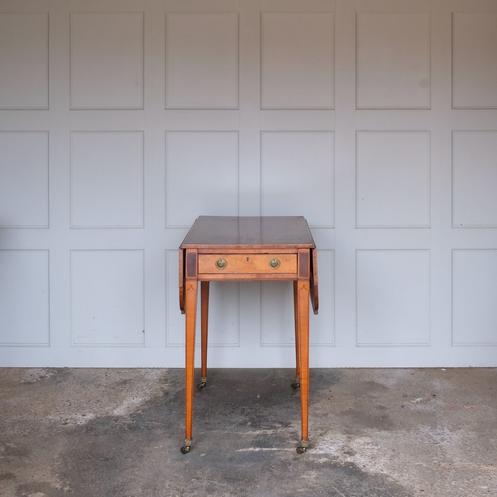 A lovely George III satinwood Pembroke table, the shaped drop leaf top with elegant crossbanding above a single end drawer with a dummy drawer on the opposing side, raised on gently tapering square legs with delicate inlay detailing over brass castors, with some gentle surface patina to the top as is commensurate with age and use, in very good condition