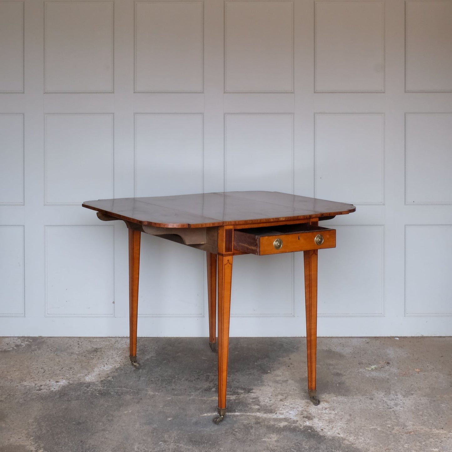 A lovely George III satinwood Pembroke table, the shaped drop leaf top with elegant crossbanding above a single end drawer with a dummy drawer on the opposing side, raised on gently tapering square legs with delicate inlay detailing over brass castors, with some gentle surface patina to the top as is commensurate with age and use, in very good condition