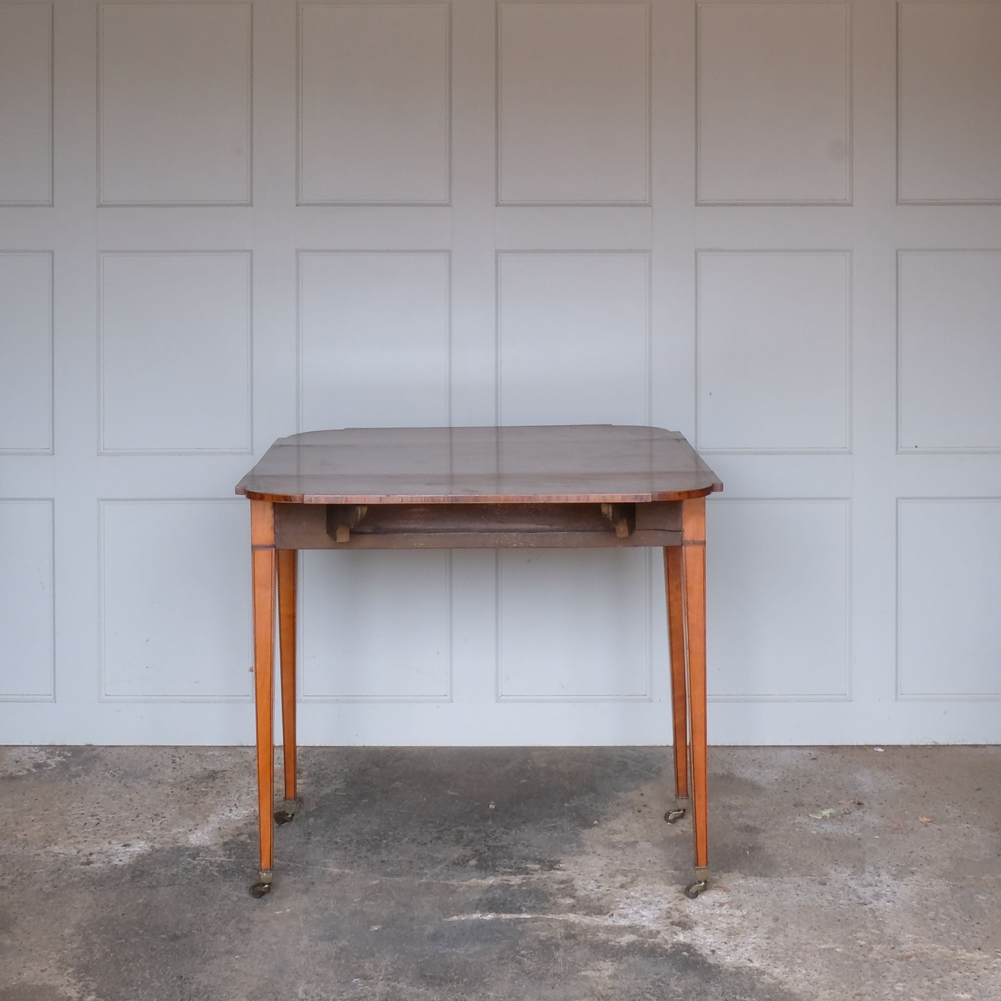 A lovely George III satinwood Pembroke table, the shaped drop leaf top with elegant crossbanding above a single end drawer with a dummy drawer on the opposing side, raised on gently tapering square legs with delicate inlay detailing over brass castors, with some gentle surface patina to the top as is commensurate with age and use, in very good condition