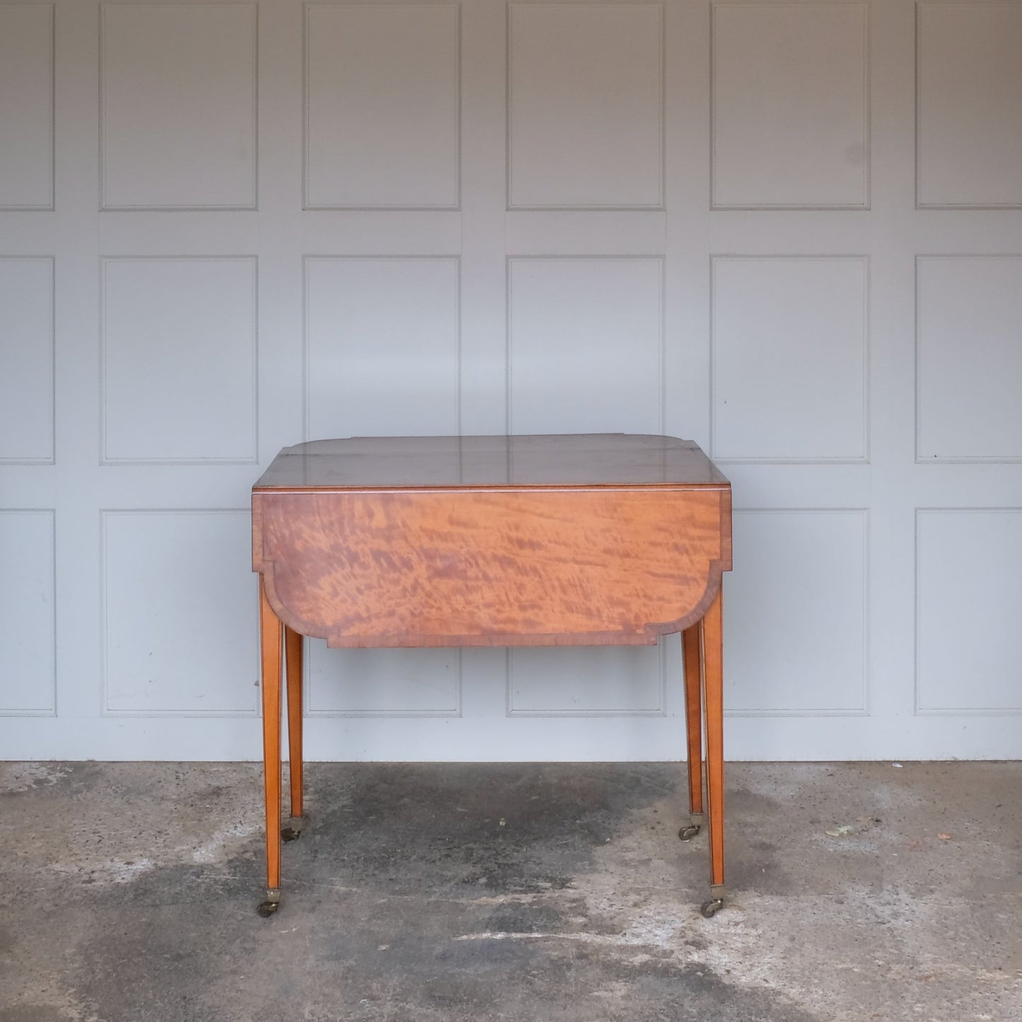 A lovely George III satinwood Pembroke table, the shaped drop leaf top with elegant crossbanding above a single end drawer with a dummy drawer on the opposing side, raised on gently tapering square legs with delicate inlay detailing over brass castors, with some gentle surface patina to the top as is commensurate with age and use, in very good condition