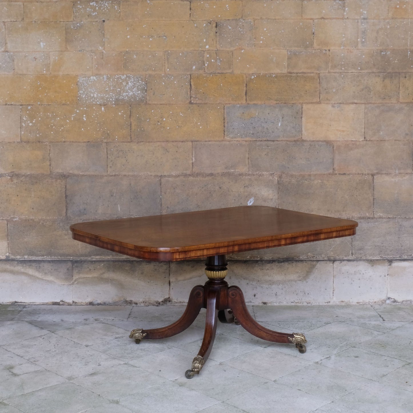 A fine Regency brass inlaid breakfast table, the rounded rectangular crossbanded tilt-top upon a turned and part gilt column support on four splayed legs with elegant tulipwood spiral inlay, showing a patina and wear commensurate with age and use, otherwise in very good condition