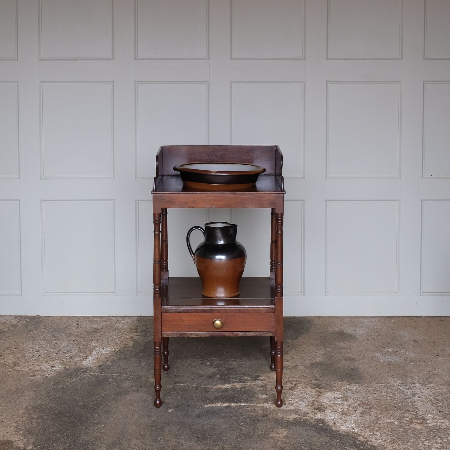 A charming early Victorian mahogany washstand, the three quarter gallery with a basin recess on turned and ringed uprights, over a single shelf with drawer over turned and ringed legs, also comprising a later stoneware basin and jug, with a gentle patina and wear commensurate with age and use, otherwise in good condition.