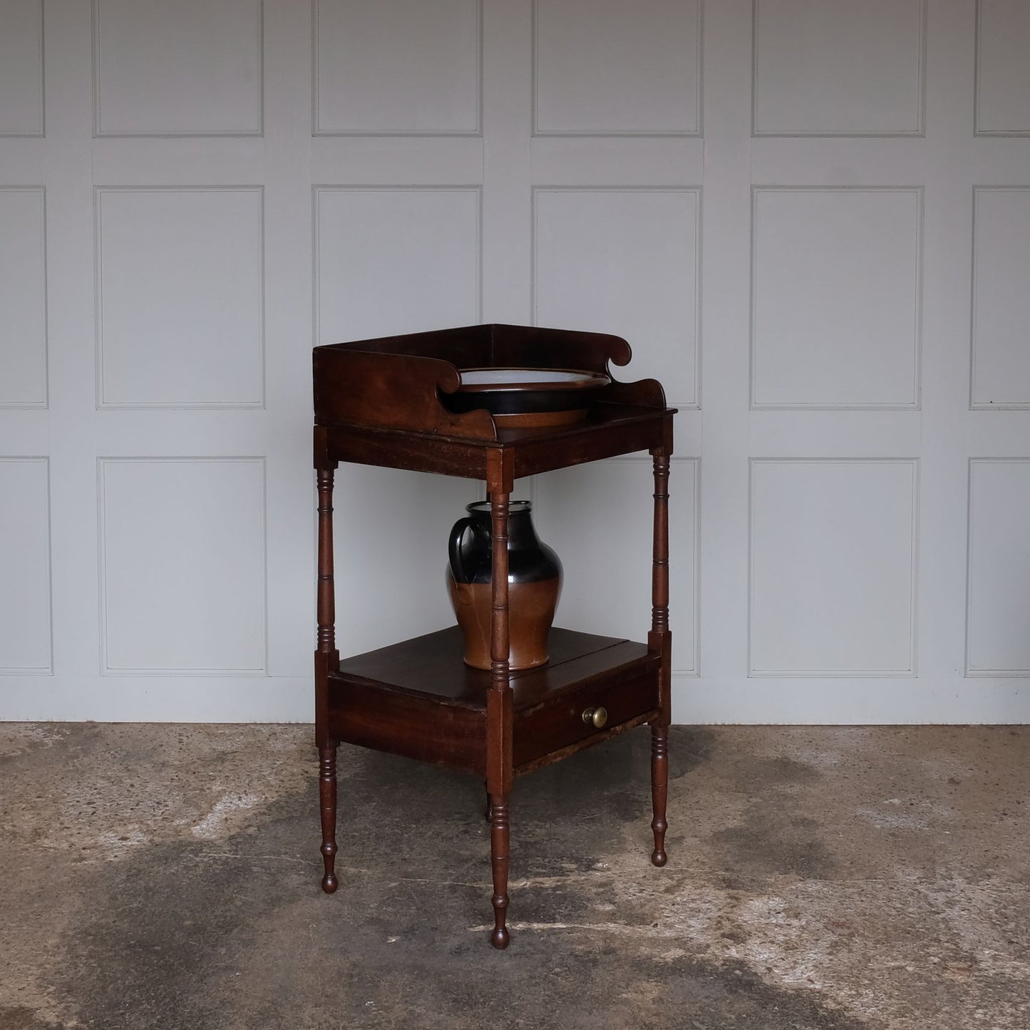 A charming early Victorian mahogany washstand, the three quarter gallery with a basin recess on turned and ringed uprights, over a single shelf with drawer over turned and ringed legs, also comprising a later stoneware basin and jug, with a gentle patina and wear commensurate with age and use, otherwise in good condition.