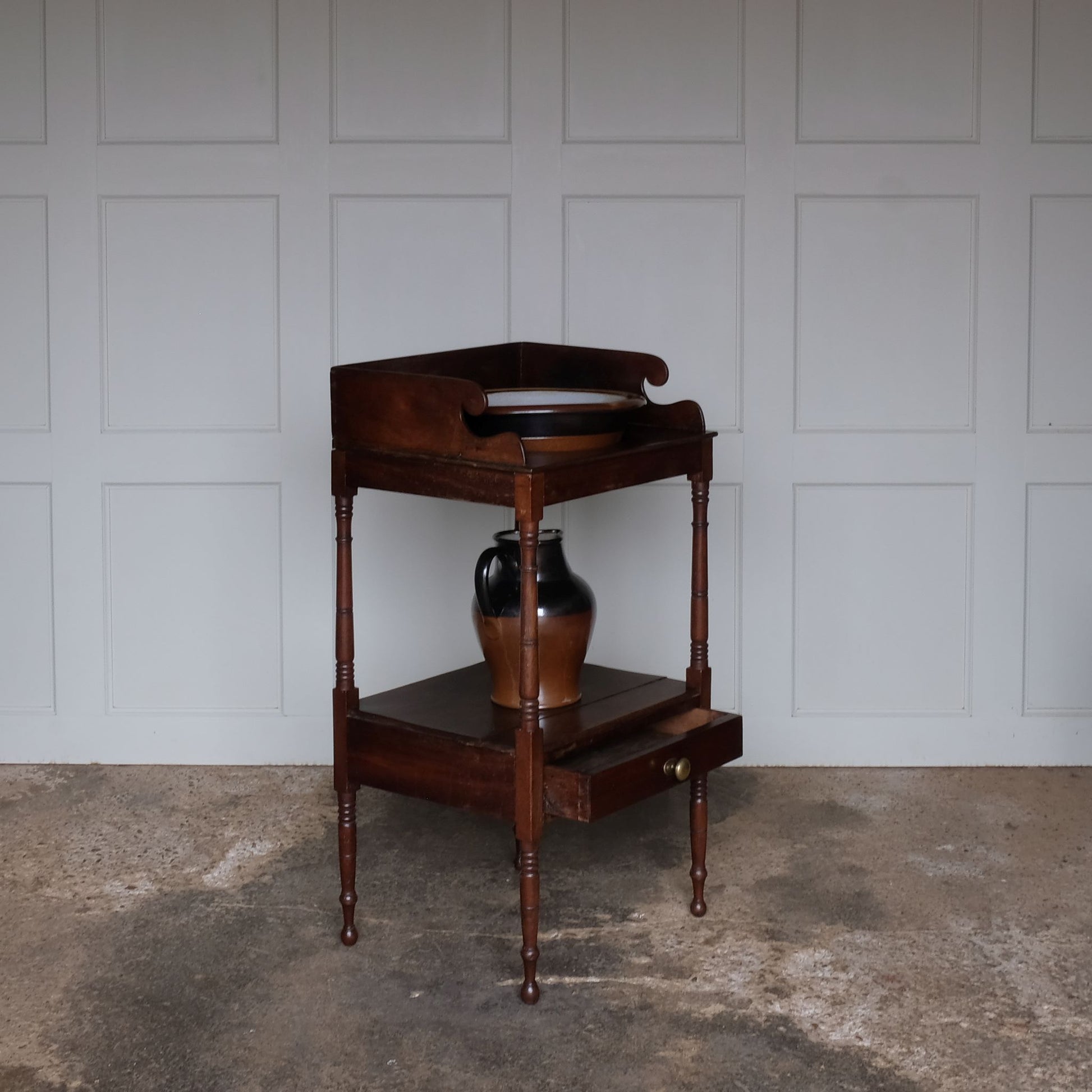 A charming early Victorian mahogany washstand, the three quarter gallery with a basin recess on turned and ringed uprights, over a single shelf with drawer over turned and ringed legs, also comprising a later stoneware basin and jug, with a gentle patina and wear commensurate with age and use, otherwise in good condition.
