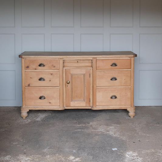 A large oak sideboard with, presumably late 19th / early 20th Century, comprising three drawers on each side with scallop cup handles, and a central drawer over a hinged cupboard door, raised on four turned bun feet. In very good, solid condition. Perfect for a kitchen or entrance hallway.