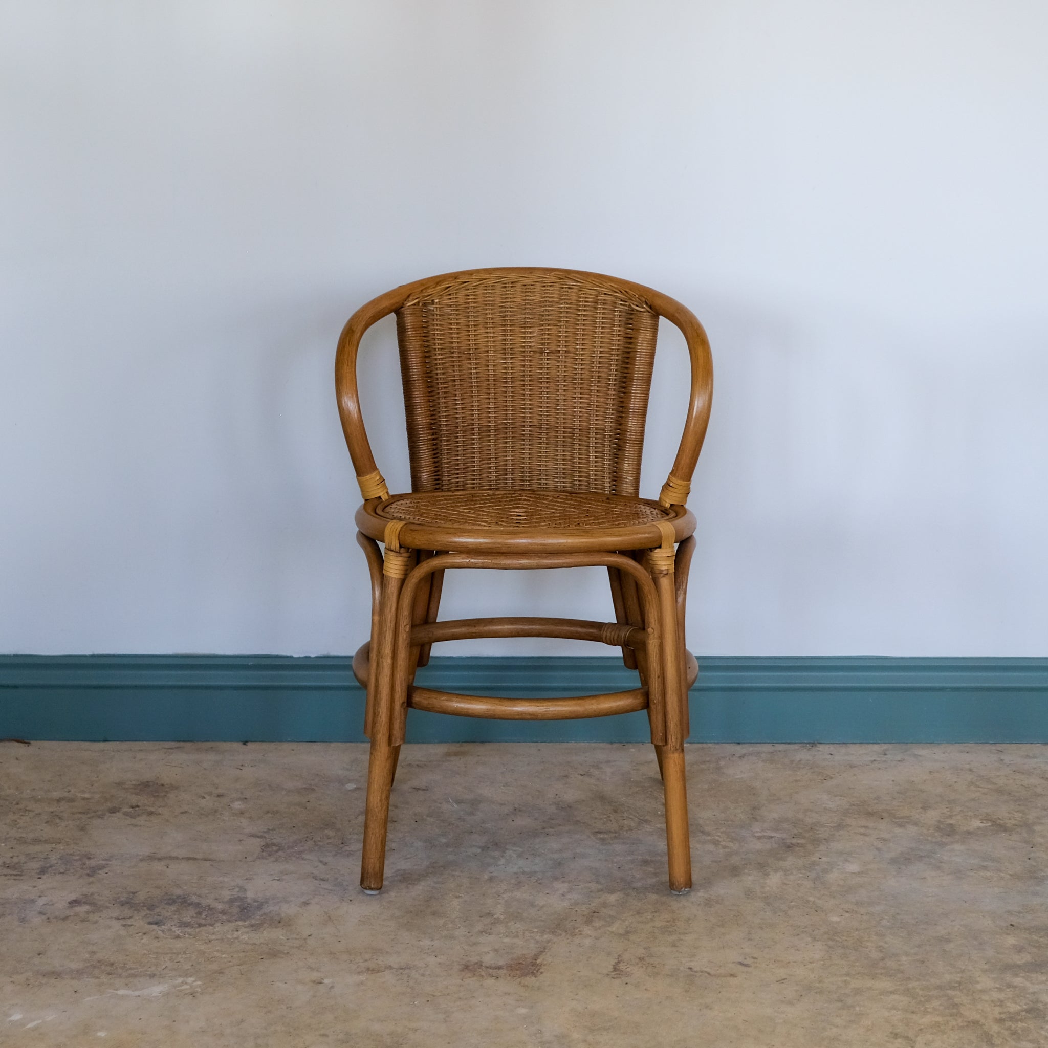 Bentwood rattan chair against a plain wall with a blue baseboard.