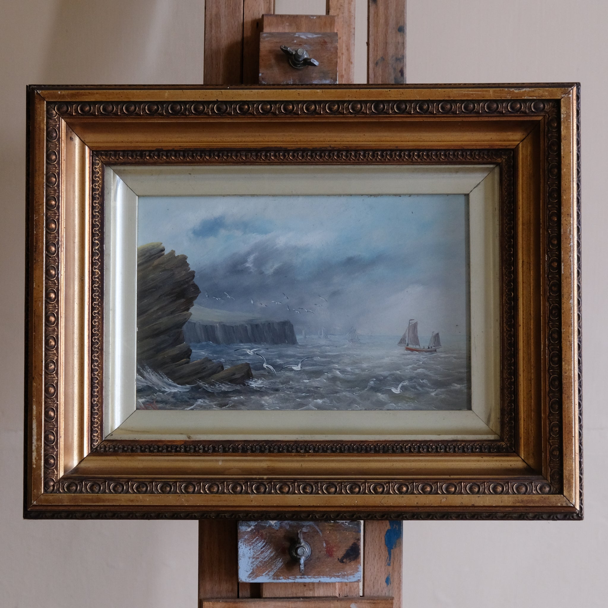 Framed painting of a seascape with cliffs and a ship on a wall.