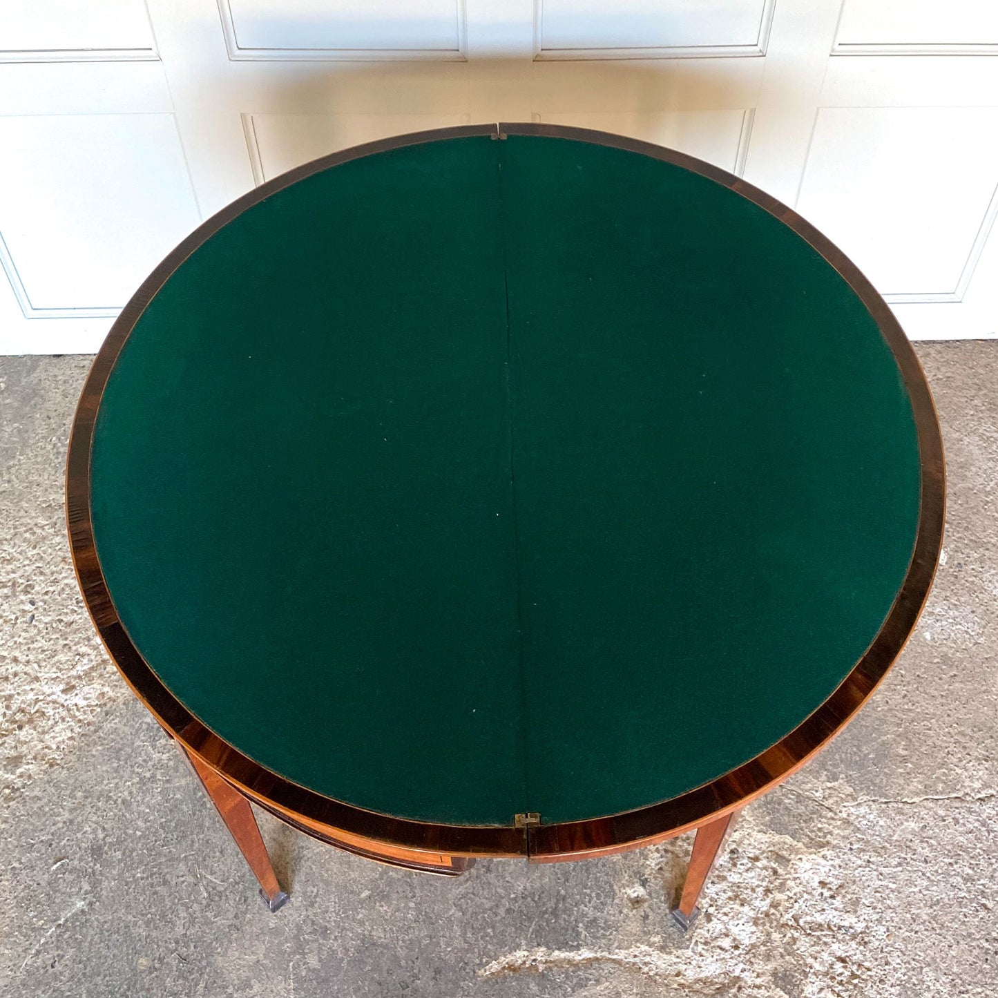 A George III satinwood and marquetry demilune folding card table, with a fold over top fitted with green baize. The top features a beautiful fan inlay and crossbanding around the outside, with the frieze incorporating purple heart crossbanding, over four elegantly tapering legs with floral painted decoration. The rear legs are hinged to swing out and support the folding top. In very good, sturdy overall condition. Would work well as a side console table, or a centre hall table.