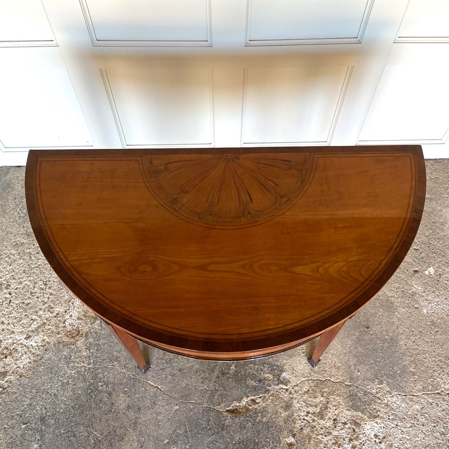 A George III satinwood and marquetry demilune folding card table, with a fold over top fitted with green baize. The top features a beautiful fan inlay and crossbanding around the outside, with the frieze incorporating purple heart crossbanding, over four elegantly tapering legs with floral painted decoration. The rear legs are hinged to swing out and support the folding top. In very good, sturdy overall condition. Would work well as a side console table, or a centre hall table.