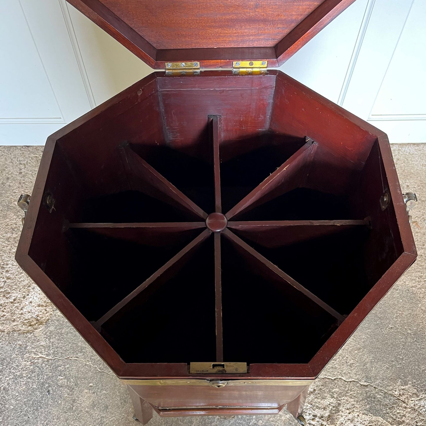 A George III mahogany octagonal brass bound wine cooler on its original stand. The hinged lid encloses an eight division interior, with brass carrying handles on the side and a fixed stand with square tapering legs on brass castors. A beautiful patina throughout. A small piece of brass trim is missing around the face of the lock, the catch of which does not completely close, leaving a gap at the front of c. 0.5cm when shut, as reflected in the price.