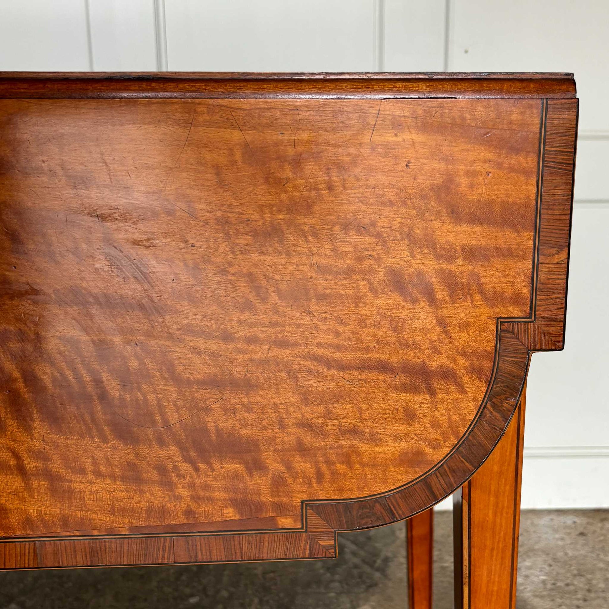 A lovely George III satinwood Pembroke table, the shaped drop leaf top with elegant crossbanding above a single end drawer with a dummy drawer on the opposing side, raised on gently tapering square legs with delicate inlay detailing over brass castors, with some gentle surface patina to the top as is commensurate with age and use, in very good condition
