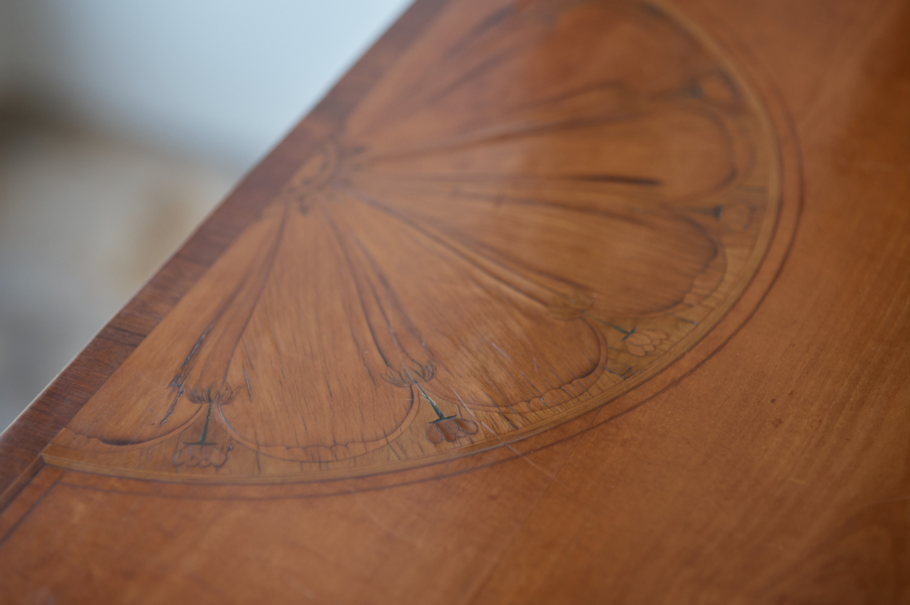 A George III satinwood and marquetry demilune folding card table, with a fold over top fitted with green baize. The top features a beautiful fan inlay and crossbanding around the outside, with the frieze incorporating purple heart crossbanding, over four elegantly tapering legs with floral painted decoration. The rear legs are hinged to swing out and support the folding top. In very good, sturdy overall condition. Would work well as a side console table, or a centre hall table.