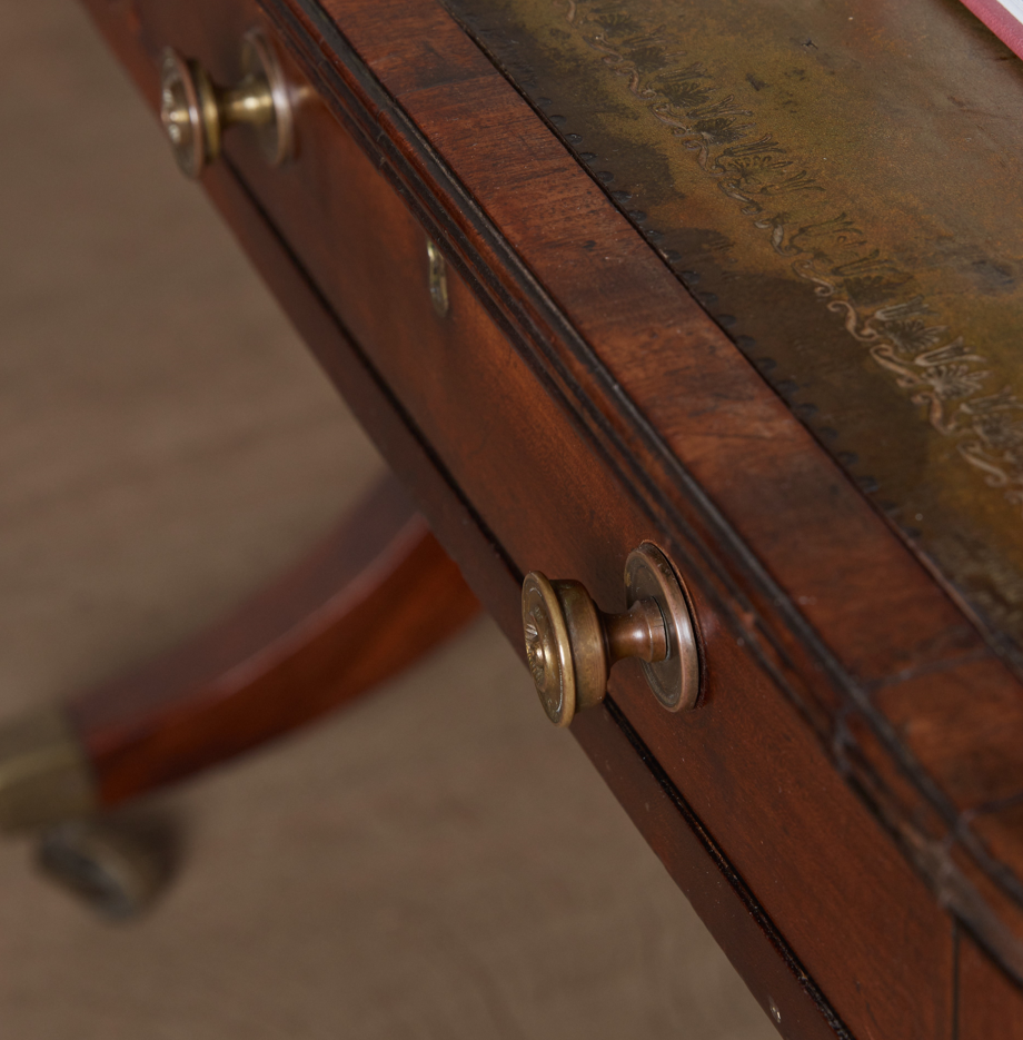 A stunning and rare George III library table, circa 1810, with original leather top with a magnificent, verdigris-like patina. A pair of frieze drawers to the front with false drawers on the reverse, over a beautifully arched crossband down to divided legs, each with a decorative scroll detailing, on period casters. The drawers can be locked with a single key. With a gentle patina commensurate with age and use, in very good condition.